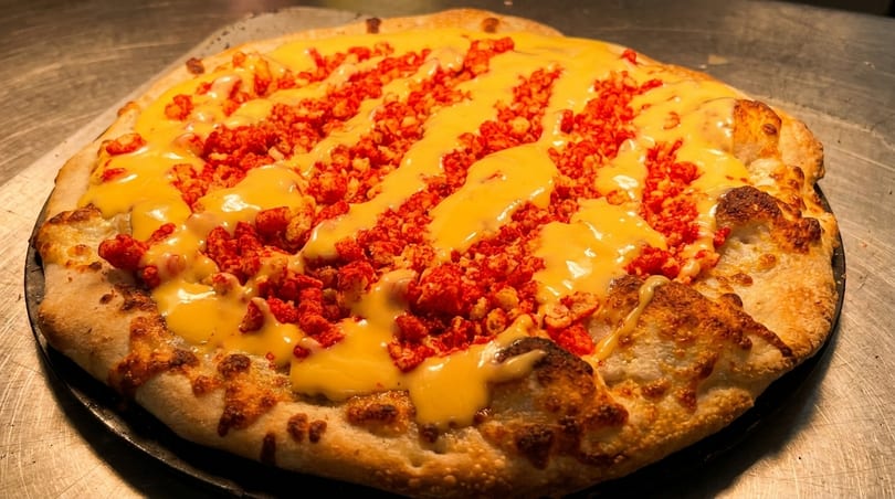 A whole pizza topped with melted cheese and bright red, crumbled spicy chips.